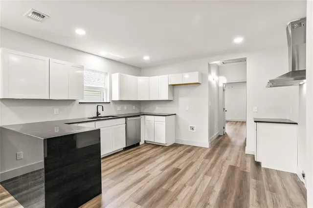 a large kitchen with a refrigerator a sink dishwasher a stove and white cabinets with wooden floor