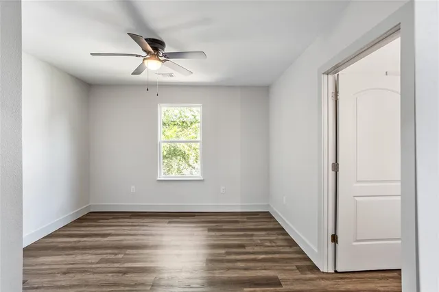 an empty room with wooden floor fan and windows