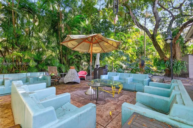 a view of a patio with couches and a table and chairs under an umbrella with large trees