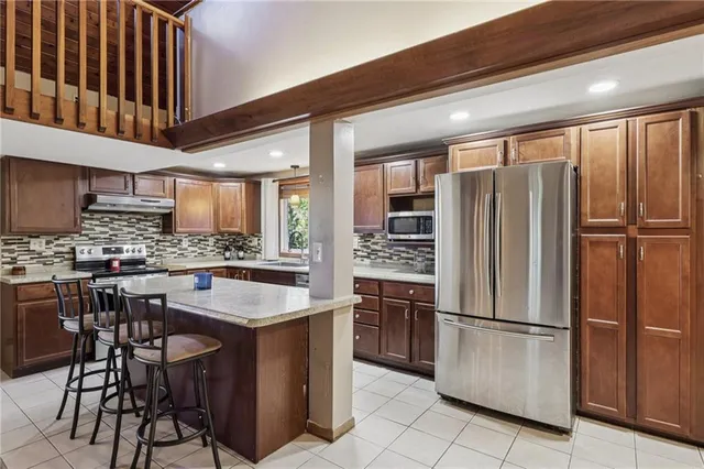 a kitchen with stainless steel appliances granite countertop a refrigerator a sink a stove and a dining table