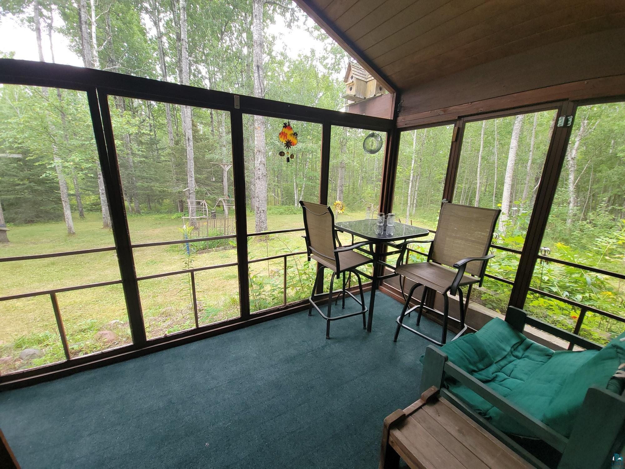 181 Linnell Road Grand Marais, MN 55604 - Photo 18 of 77 Screened porch with wood-finish ceiling, green carpeting, and exterior landscaping