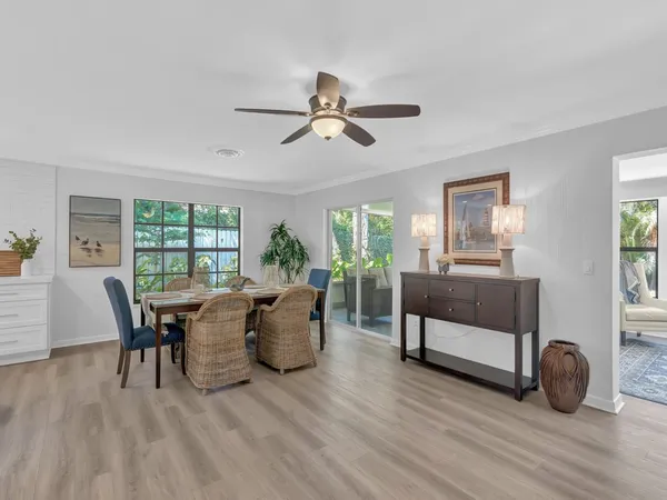 a dining room with wooden floor a chandelier fan a glass table and windows