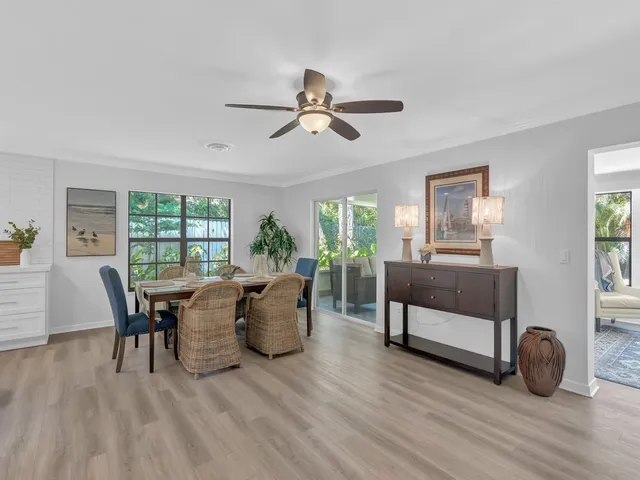 a dining room with wooden floor a chandelier fan a glass table and windows