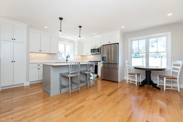 a kitchen with kitchen island a dining table chairs refrigerator and wooden floor