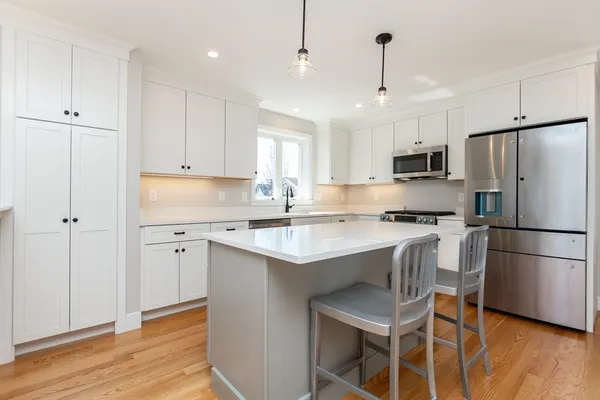 a kitchen with kitchen island granite countertop a sink stove a refrigerator and white cabinets with wooden floor