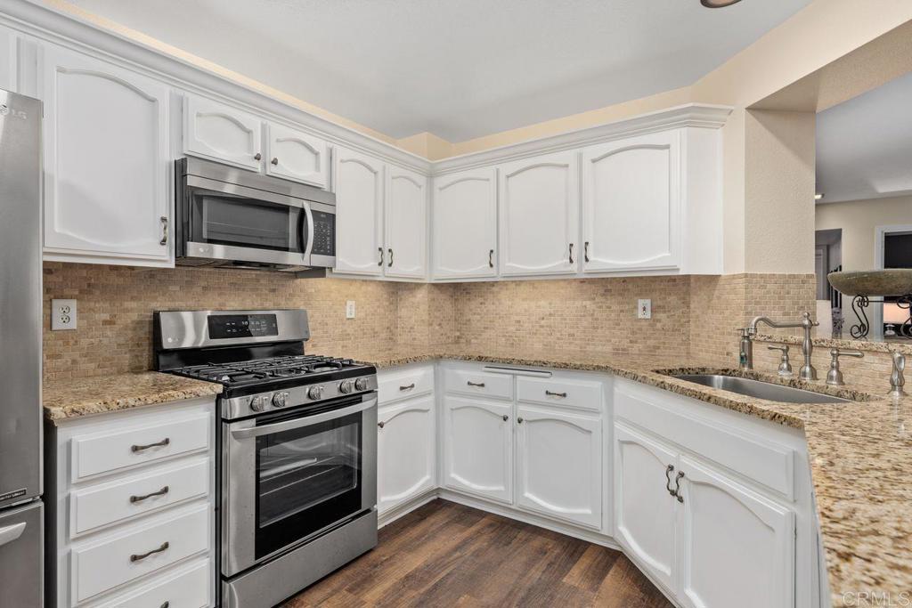 7325 Lantana Terrace Carlsbad, CA 92011 - Photo 11 of 36 a kitchen with granite countertop white cabinets sink and stainless steel appliances