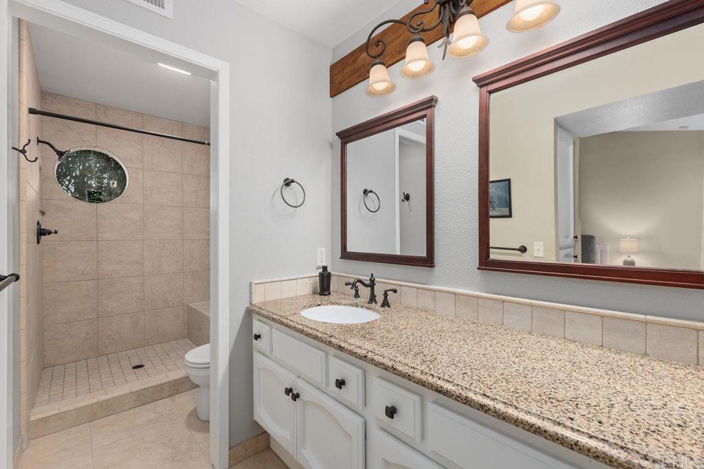 7325 Lantana Terrace Carlsbad, CA 92011 - Photo 19 of 36 a bathroom with a granite countertop sink a mirror a shower and a bathtub