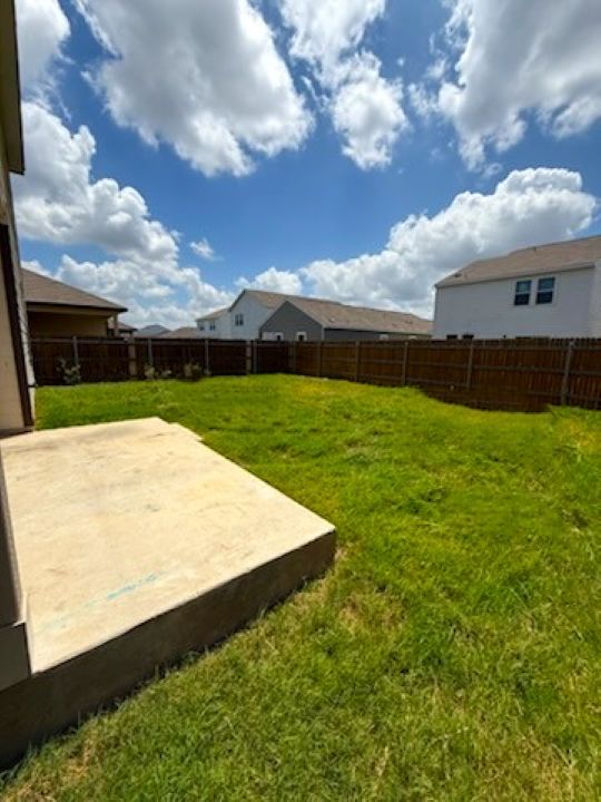 129 Perfect World Loop Jarrell, TX 76537 - Photo 28 of 31 A spacious backyard enclosed by a wooden fence, featuring a concrete patio perfect for outdoor living.