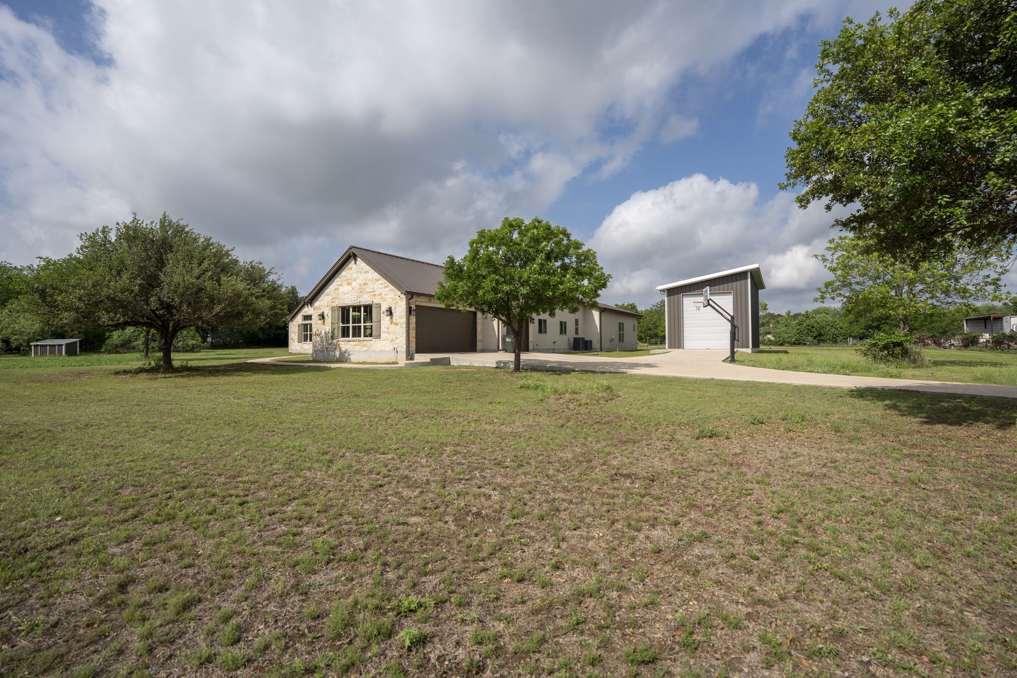 16202 Remuda Trail Buda, TX 78610 - Photo 33 of 40 The property features a stone exterior with a dark roof, an attached three car garage, and a separate 45’ x 20’ insulated metal building