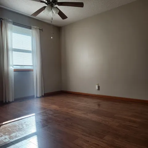 an empty room with wooden floor chandelier fan and windows