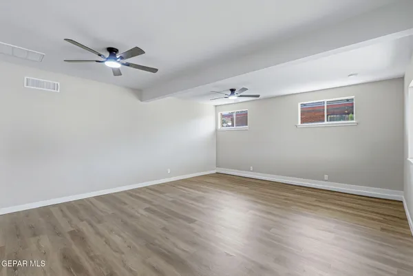 an empty room with wooden floor a ceiling fan & windows