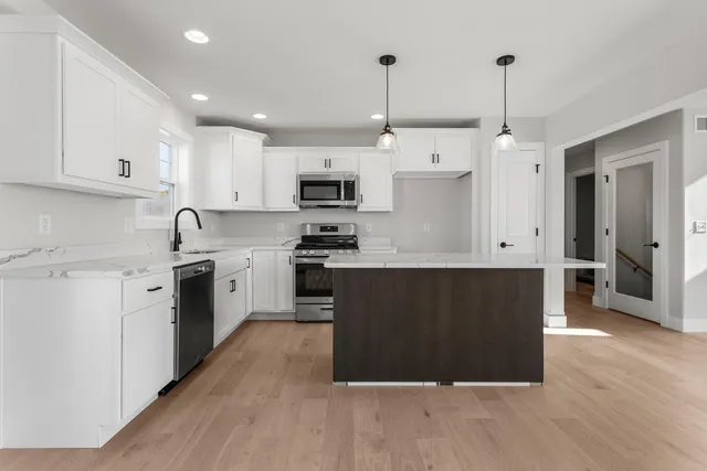 a large kitchen with stainless steel appliances granite countertop a stove a sink a refrigerator and white cabinets with wooden floor