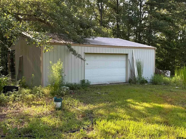 a backyard of a house with plants and large tree