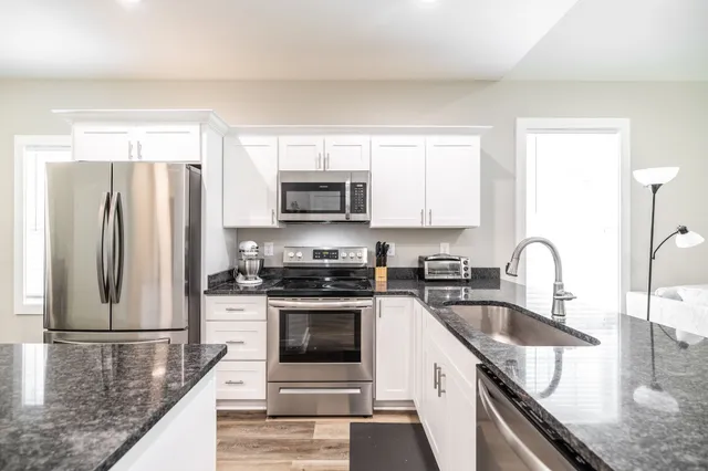 a kitchen with stainless steel appliances granite countertop a sink a stove a refrigerator a microwave with wooden cabinets and floor