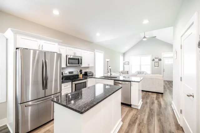 a kitchen with stainless steel appliances granite countertop a refrigerator a sink dishwasher a stove and white countertops with wooden floor