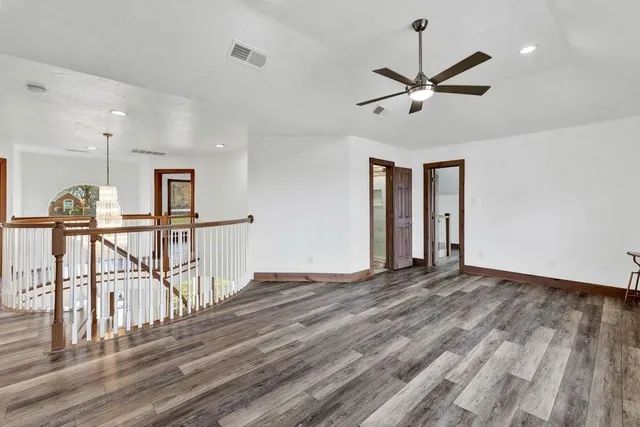 an empty room with wooden floor ceiling fan and windows