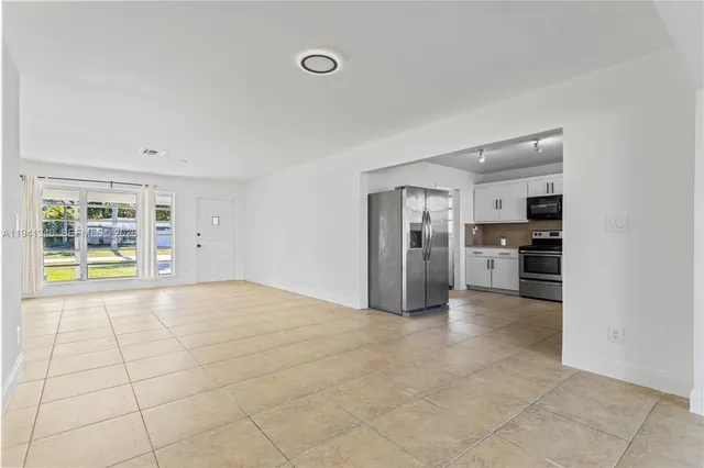a view of an empty room with kitchen and window