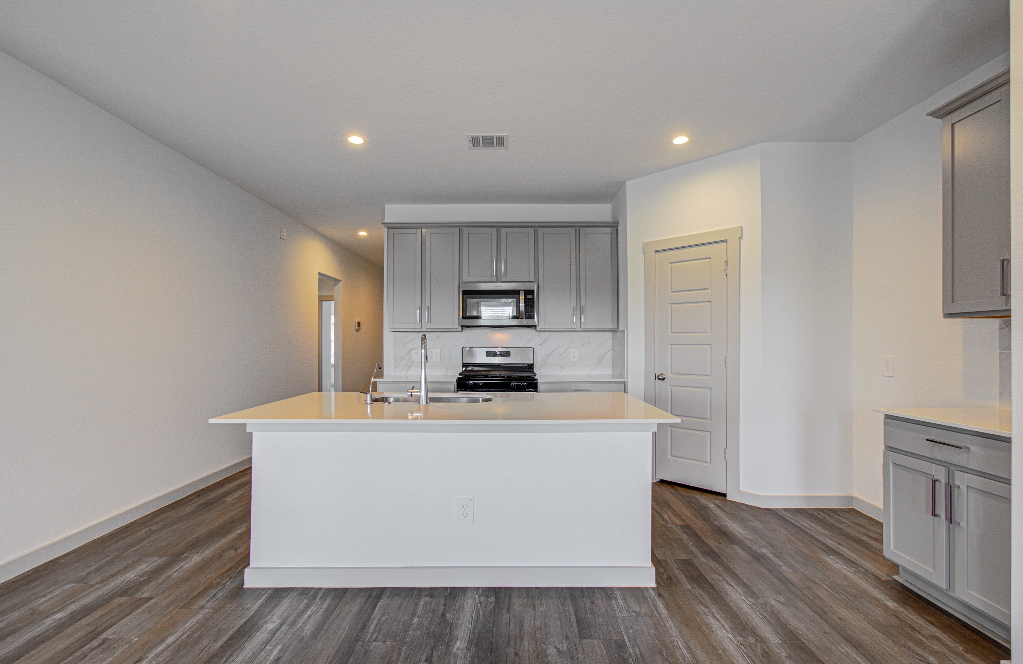 7903 Wrangler Shack Lane Rosharon, TX 77583 - Photo 15 of 29 Discover a modern kitchen featuring sleek gray cabinetry, stainless steel appliances, and a spacious island with a sink, all set within a bright, open layout with wood-style flooring and recessed lighting—a perfect blend of style and functionality.