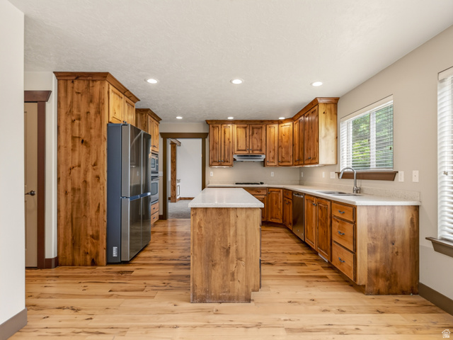 1279 West 1500th Street North Mapleton, UT 84664 - Photo 18 of 83 Spacious kitchen featuring extensive wood-finish cabinetry, a large kitchen island with a light-toned countertop, stainless steel appliances, recessed lighting, and wood-finish flooring