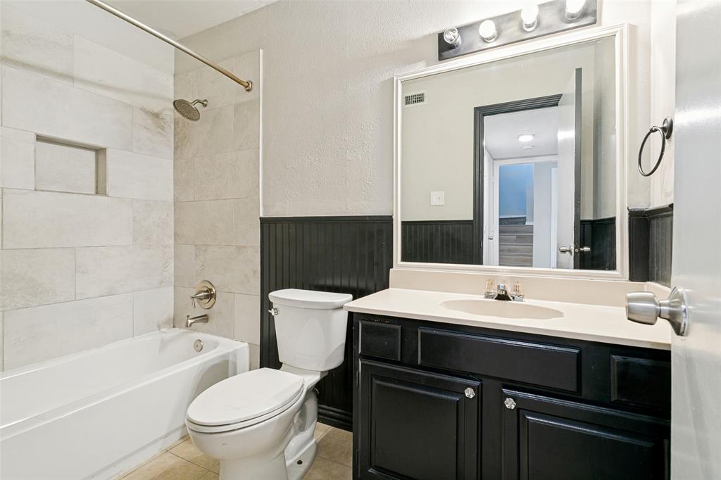 1712 East Peters Colony Road Carrollton, TX 75007 - Photo 16 of 25 Bathroom featuring a white tub, light-toned tile surround with built-in niche, dark wainscoting, and a single vanity with a light countertop and dark cabinetry