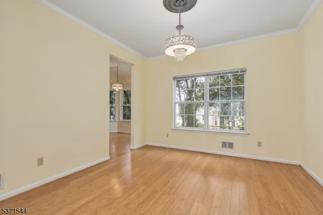 an empty room with wooden floor chandelier and windows