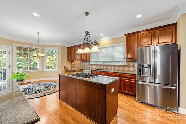 a kitchen with stainless steel appliances granite countertop a refrigerator a sink a stove and a wooden floors