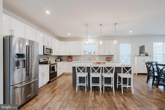 a kitchen with stainless steel appliances granite countertop a dining table chairs refrigerator and sink