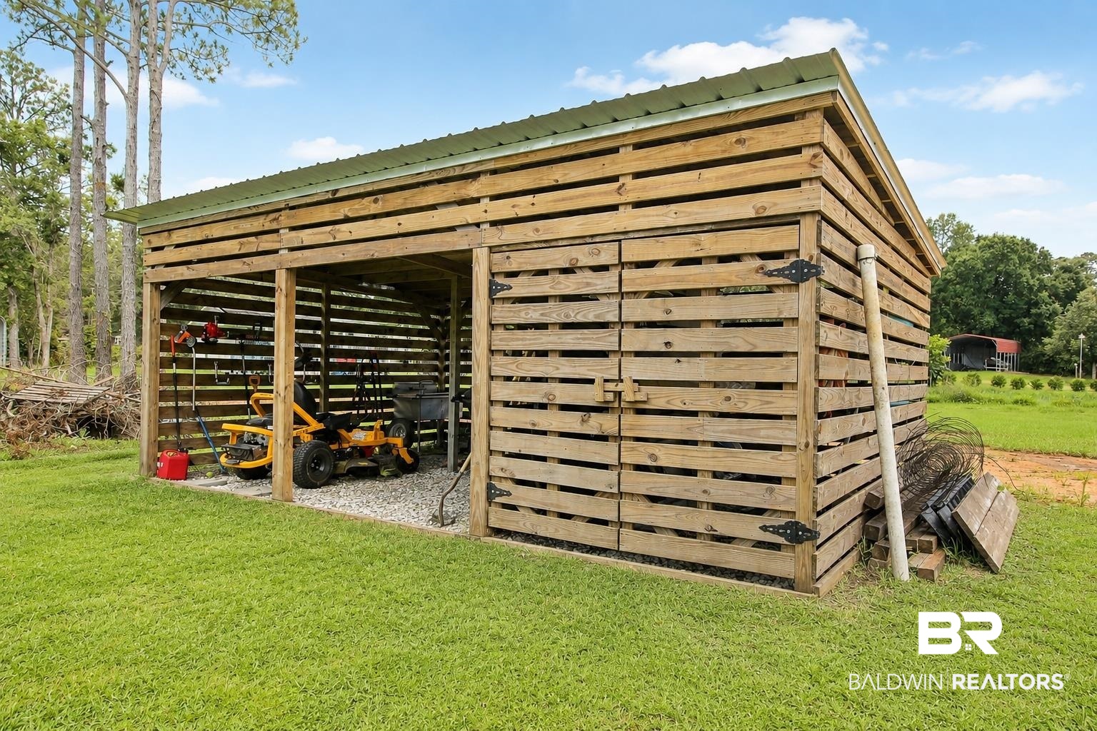 9825 Wolf Creek Ridge Elberta, AL 36530 - Photo 68 of 76 Rustic wood-slat shed with a green metal roof, featuring an open bay with gravel flooring, and an enclosed storage area with double wooden doors