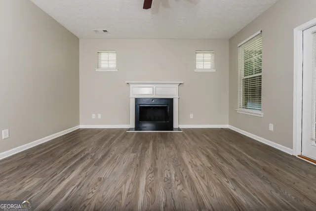 an empty room with wooden floor fireplace and windows