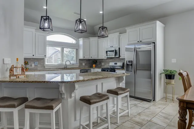 a kitchen with stainless steel appliances granite countertop a sink a stove a refrigerator and a dining table with chairs