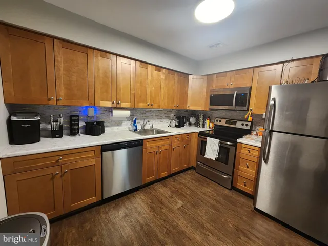 a kitchen with granite countertop a refrigerator a stove top oven a sink dishwasher and wooden cabinets with wooden floor