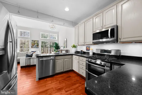 a kitchen with stainless steel appliances granite countertop wooden cabinets a sink a stove a dining table and chairs