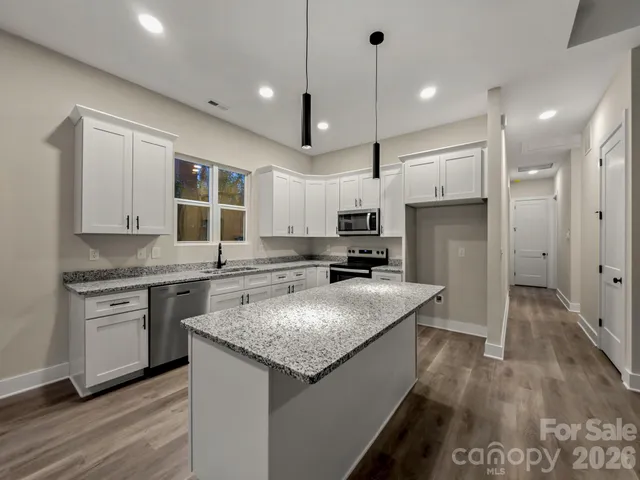 a kitchen with stainless steel appliances granite countertop a sink a stove a refrigerator and island with wooden floor