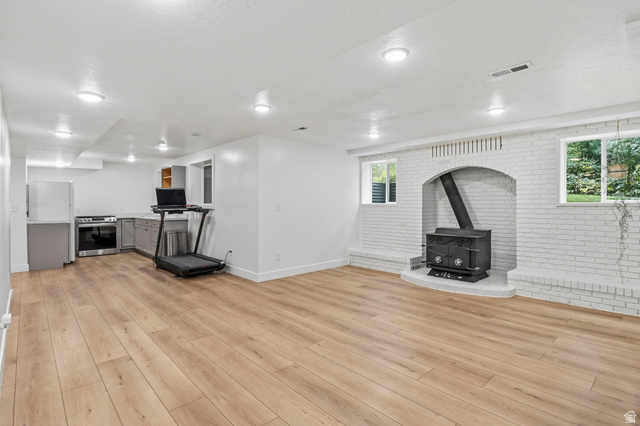 4150 Dover Lane Provo, UT 84604 - Photo 27 of 44 Spacious open-concept living area featuring wood-finish flooring, recessed lighting, and a white brick-faced hearth with a freestanding stove