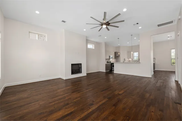 a view of an empty room with wooden floor and a kitchen