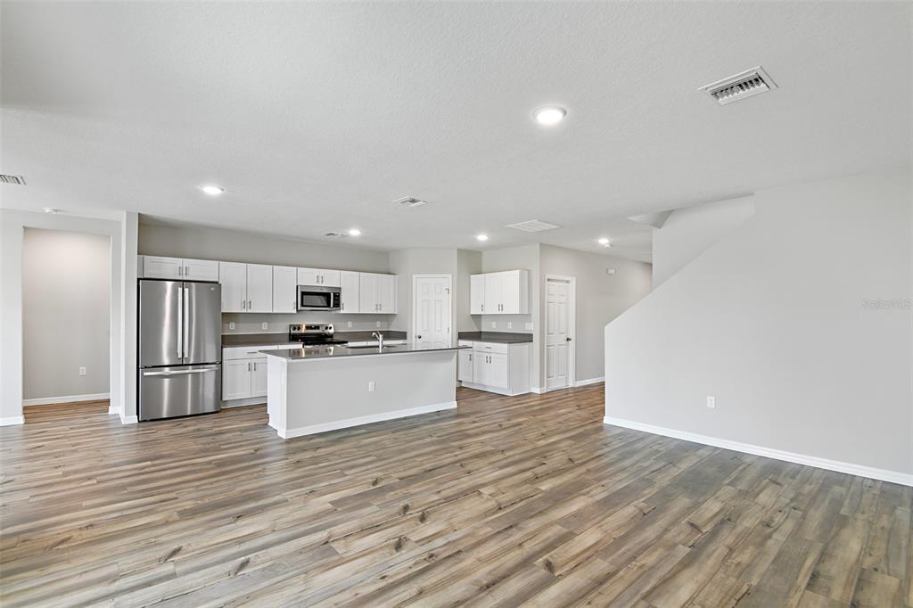4385 Prairie Run Haines City, FL 33844 - Photo 4 of 25 a large kitchen with kitchen island a sink a stove a refrigerator and white cabinets with wooden floor