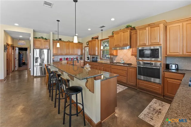 a kitchen with stainless steel appliances granite countertop a stove top oven a sink dishwasher a dining table and chairs with wooden floor