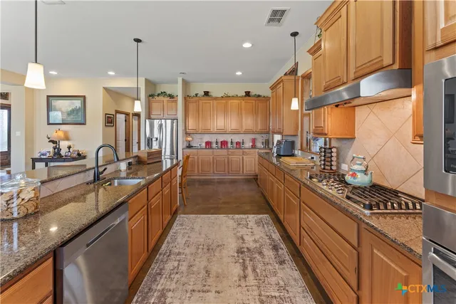 a large kitchen with stainless steel appliances kitchen island granite countertop a large counter top a stove a sink and a refrigerator