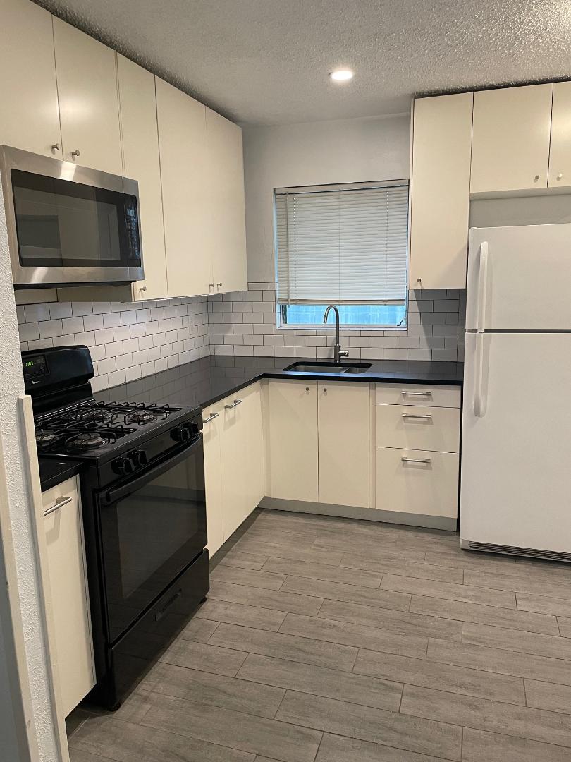 6000 Grover Avenue, Unit A Austin, TX 78757 - Photo 4 of 18 Kitchen featuring black range with gas cooktop, freestanding refrigerator, dark countertops, stainless steel microwave, and a textured ceiling