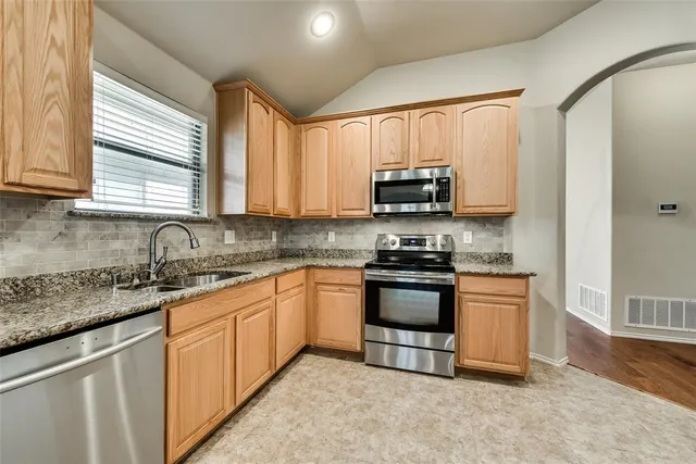 a kitchen with stainless steel appliances granite countertop wooden cabinets a stove a sink and a window