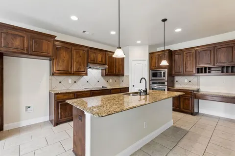 a large kitchen with granite countertop a sink a counter top space appliances and cabinets