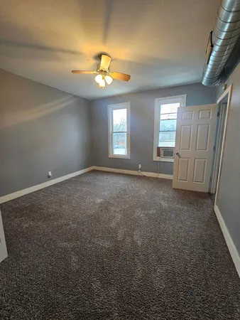 an empty room with a chandelier fan and windows