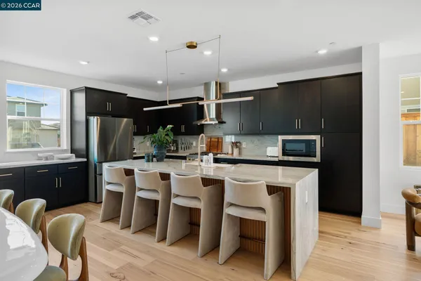 a kitchen with stainless steel appliances kitchen island granite countertop a refrigerator a stove a sink a dining table and chairs with wooden floor