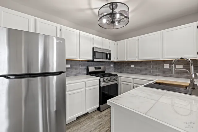 a kitchen with stainless steel appliances a refrigerator a sink and white cabinets