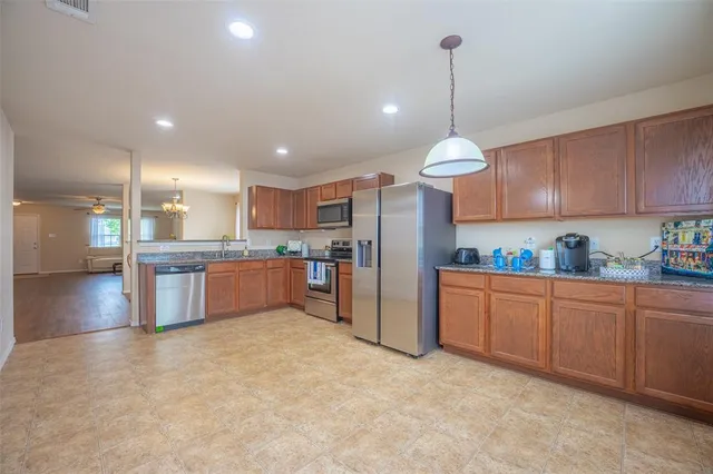 a kitchen with stainless steel appliances granite countertop a refrigerator a sink dishwasher a oven and a dining table with wooden floor