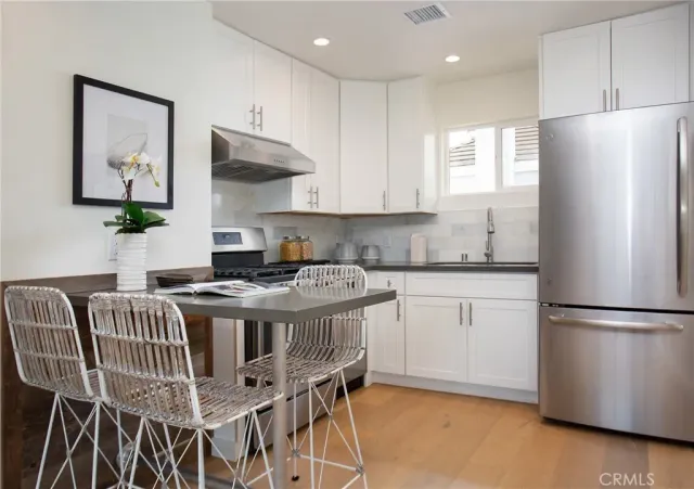 a kitchen with stainless steel appliances granite countertop a stove a refrigerator a sink a dining table and chairs with wooden floor