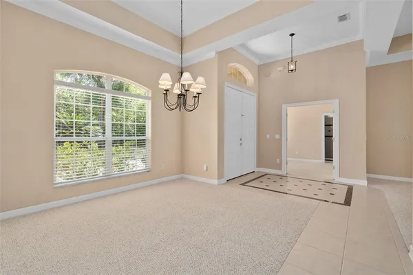 a view of an empty room with a chandelier fan and kitchen view