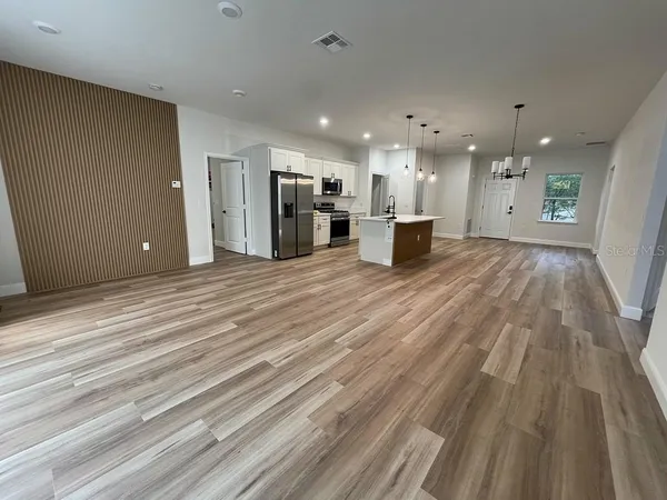 a kitchen with stainless steel appliances a stove top oven a sink dishwasher a refrigerator and a dining table with wooden floor