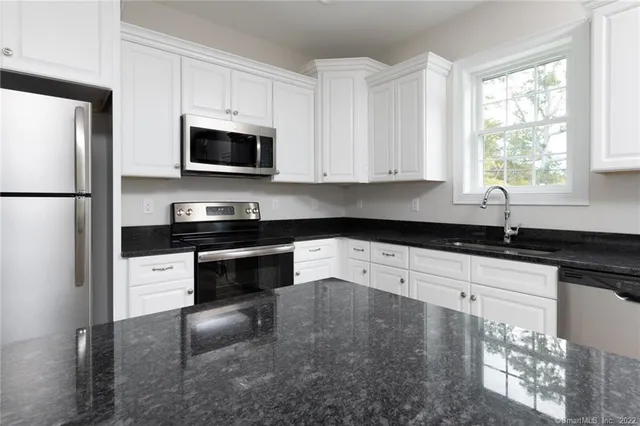 a white kitchen with stainless steel appliances granite countertop a stove a sink and a refrigerator