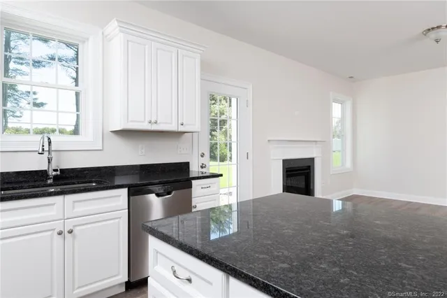 a kitchen with granite countertop a sink dishwasher a stove and white cabinets with wooden floor
